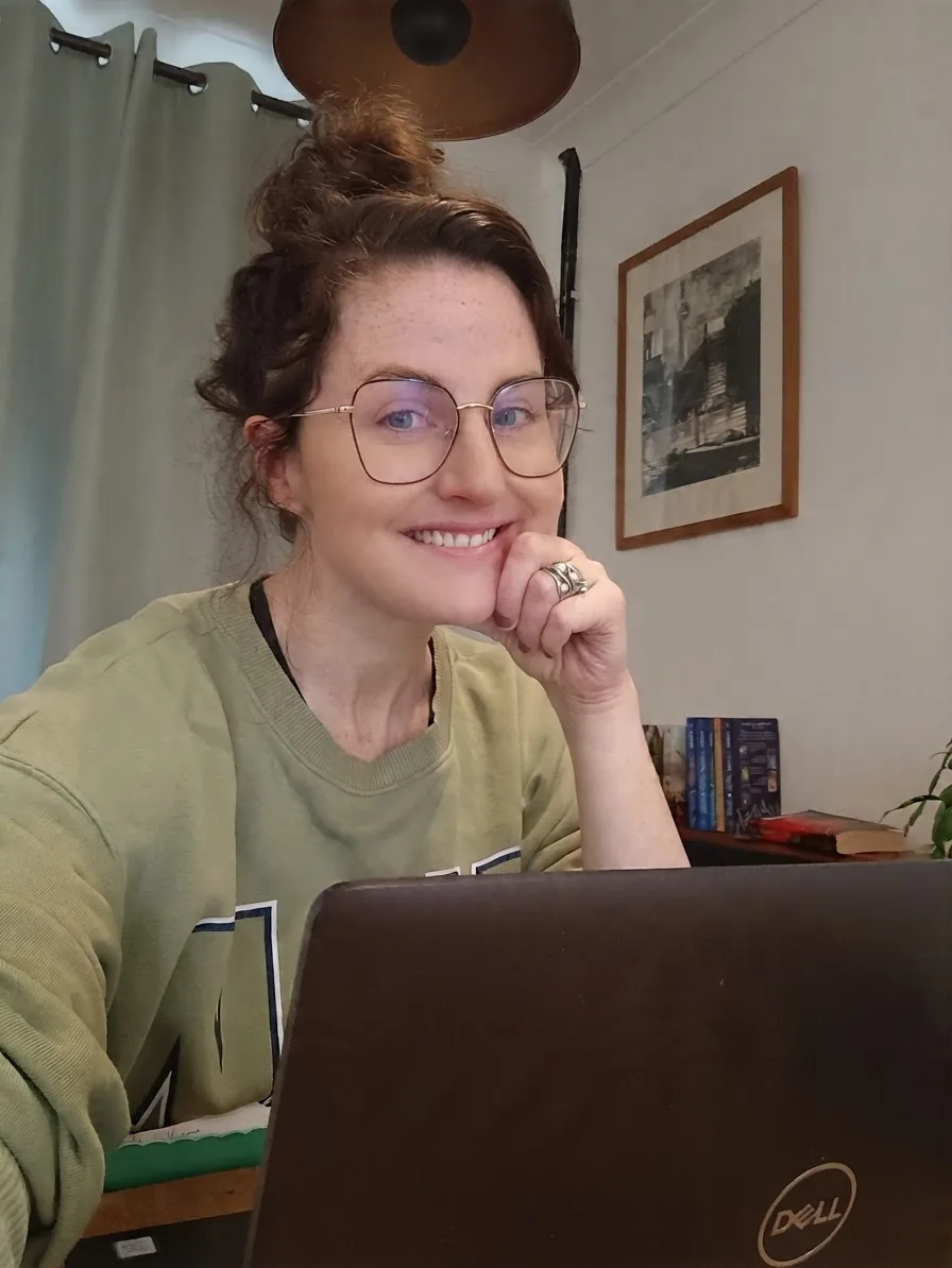 Brickify's founder smiling at her kitchen table, chin resting on her hand, behind a laptop.
